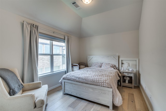 bedroom with light wood-style floors, baseboards, vaulted ceiling, and visible vents