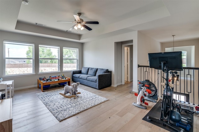living area with baseboards, a ceiling fan, a tray ceiling, and wood finished floors