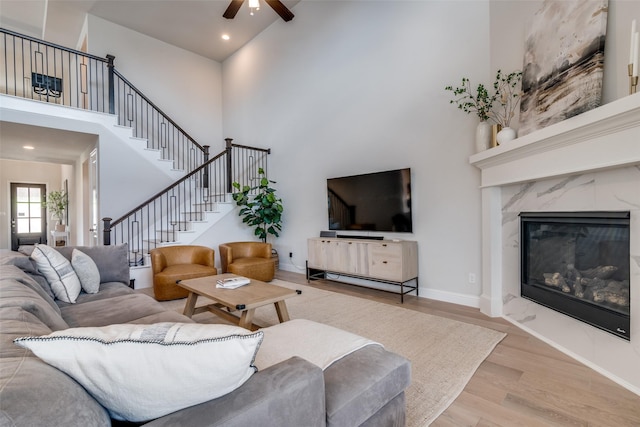 living area with ceiling fan, a towering ceiling, wood finished floors, baseboards, and stairs