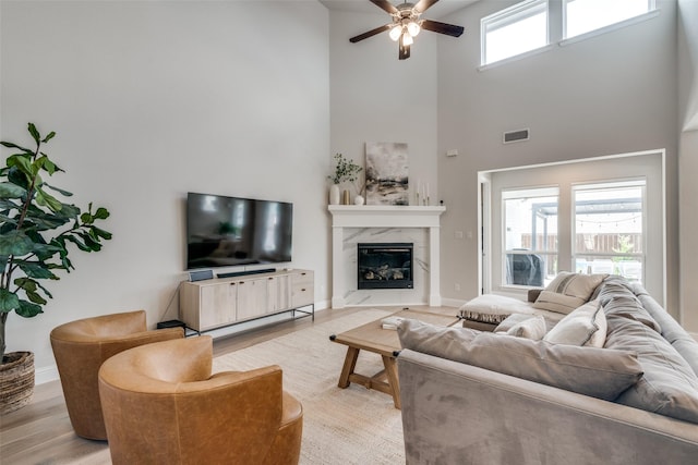 living area with a ceiling fan, visible vents, a high end fireplace, wood finished floors, and a high ceiling