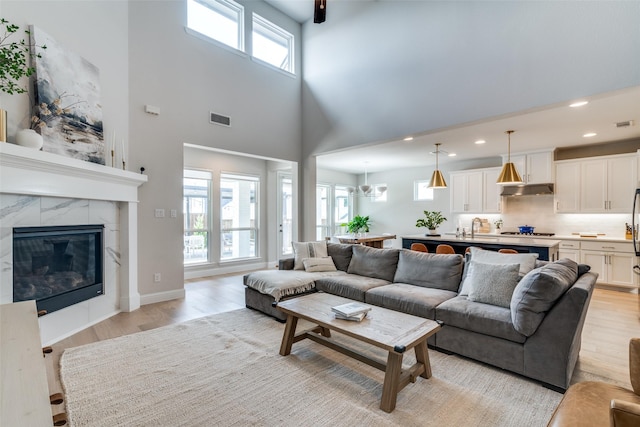 living room with visible vents, a fireplace, light wood-style floors, a high ceiling, and recessed lighting