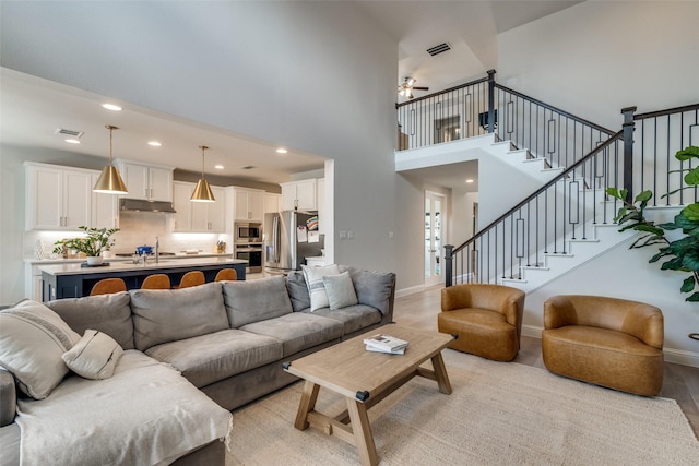 living area featuring visible vents, stairs, a towering ceiling, ceiling fan, and light wood finished floors