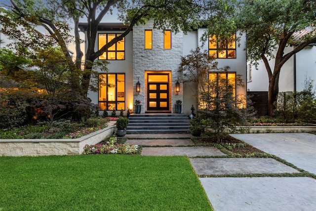 modern home featuring stone siding, stucco siding, and a front lawn