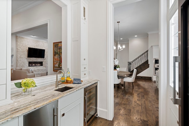 bar with beverage cooler, a sink, stairs, crown molding, and a fireplace