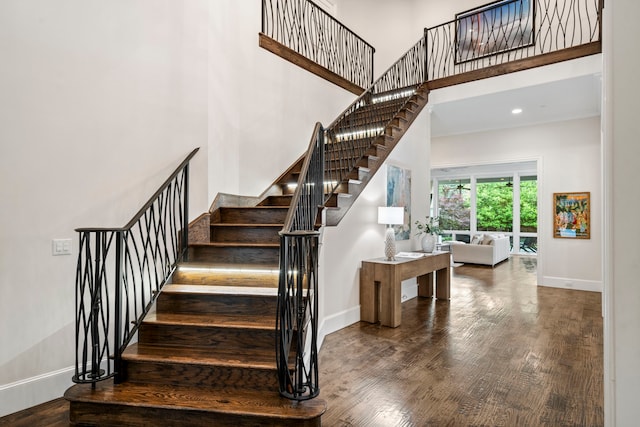 stairway featuring wood finished floors, baseboards, and a high ceiling