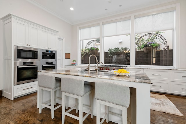 kitchen featuring light stone countertops, a sink, a kitchen breakfast bar, crown molding, and white cabinets