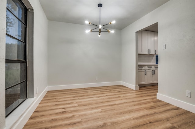 unfurnished dining area with light wood finished floors, an inviting chandelier, and baseboards