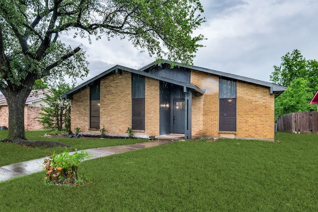 mid-century modern home with brick siding, a front lawn, and fence