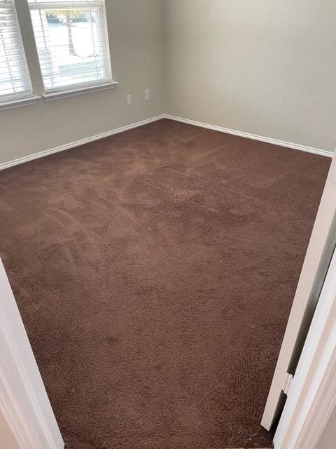 unfurnished room featuring dark colored carpet and baseboards
