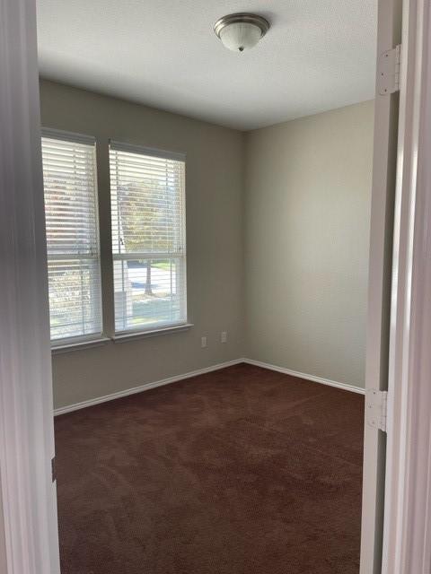 spare room with baseboards and dark carpet