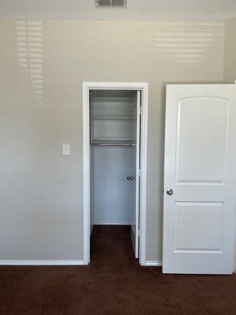 unfurnished bedroom with a closet, baseboards, dark colored carpet, visible vents, and a spacious closet