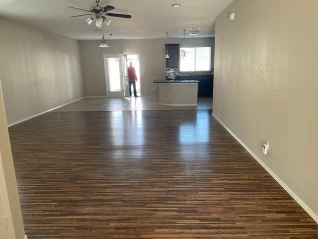 empty room with dark wood-type flooring, baseboards, a ceiling fan, and visible vents