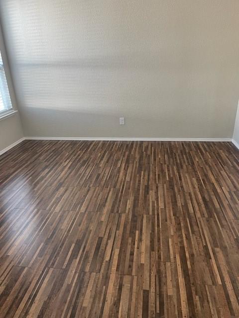 spare room with baseboards and dark wood-style floors