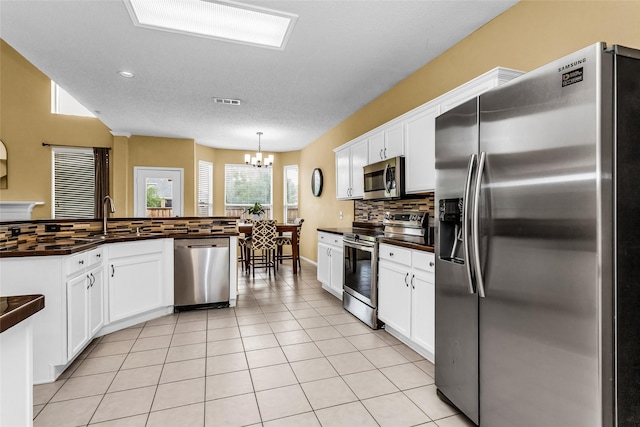kitchen with a sink, tasteful backsplash, an inviting chandelier, white cabinets, and appliances with stainless steel finishes