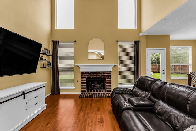 living room with baseboards, a towering ceiling, a brick fireplace, and dark wood-style floors