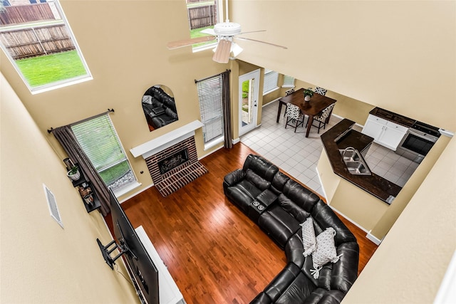 living area with wood finished floors, a towering ceiling, ceiling fan, baseboards, and a tile fireplace