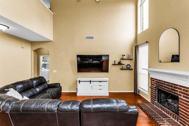 living area featuring wood finished floors, visible vents, arched walkways, plenty of natural light, and a high ceiling