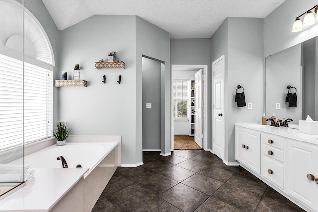 bathroom with a garden tub, a textured ceiling, baseboards, vaulted ceiling, and vanity
