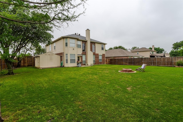 rear view of property featuring a lawn, a shed, a fire pit, and a fenced backyard