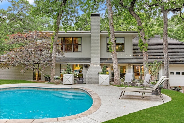 rear view of property featuring brick siding, a patio, a chimney, and an outdoor pool