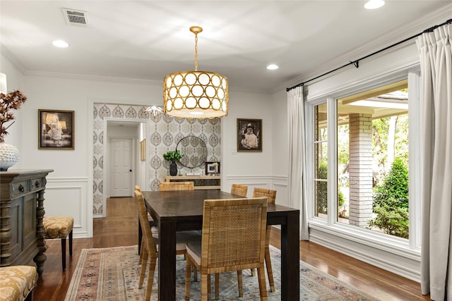 dining area with crown molding, a decorative wall, visible vents, and wood finished floors