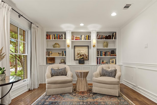 living area with wood finished floors, plenty of natural light, visible vents, and built in shelves
