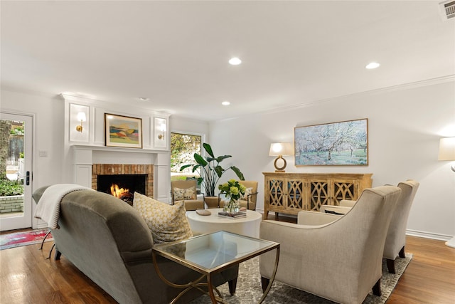 living room featuring wood finished floors, ornamental molding, visible vents, recessed lighting, and a fireplace