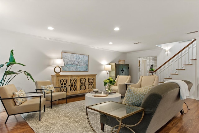 living room with visible vents, wood finished floors, ornamental molding, and stairs