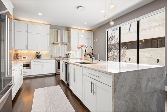 kitchen with wall chimney range hood, a sink, dark wood finished floors, appliances with stainless steel finishes, and tasteful backsplash