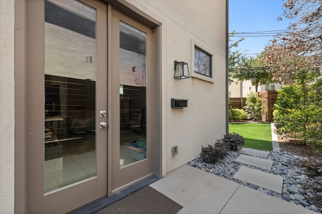 entrance to property with stucco siding, french doors, and fence
