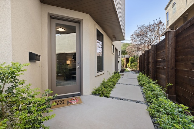 doorway to property featuring stucco siding and fence