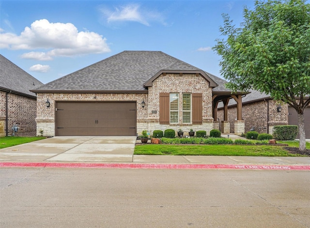 french country inspired facade featuring roof with shingles, stone siding, brick siding, driveway, and a garage