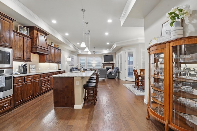 kitchen with a breakfast bar, premium range hood, open floor plan, stainless steel appliances, and a fireplace