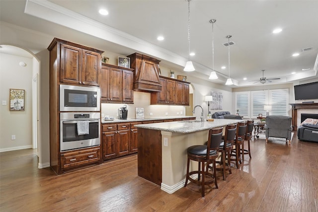kitchen with arched walkways, a raised ceiling, custom exhaust hood, and open floor plan