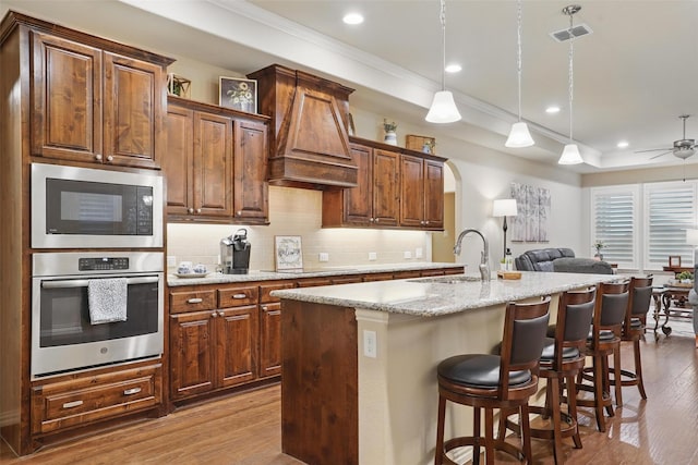 kitchen with a sink, premium range hood, oven, open floor plan, and built in microwave