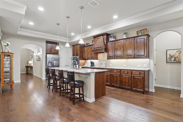kitchen featuring a breakfast bar area, a center island with sink, visible vents, arched walkways, and custom exhaust hood