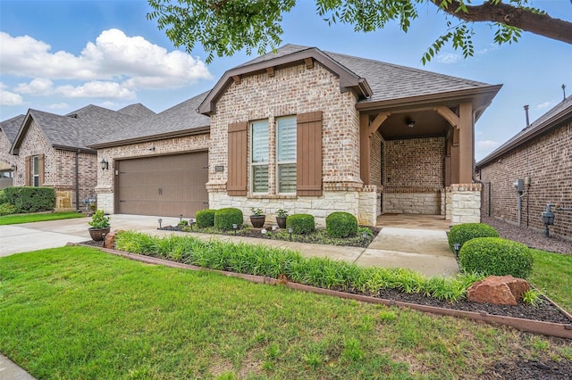 french country style house with driveway, brick siding, a shingled roof, stone siding, and a front lawn