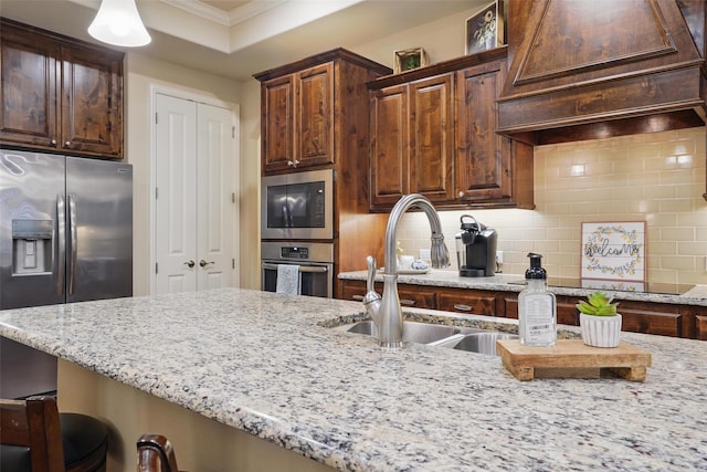 kitchen featuring a sink, stainless steel appliances, a breakfast bar area, decorative backsplash, and light stone countertops