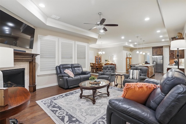 living area featuring ceiling fan with notable chandelier, visible vents, dark wood-style floors, a raised ceiling, and baseboards