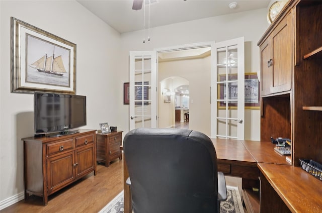 office area with ceiling fan, arched walkways, and light wood-style floors