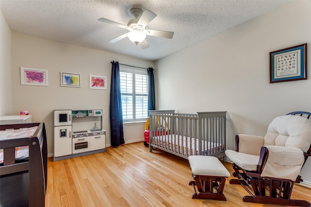 6712 Bluffview Dr, Fort Worth, TX 76132 - bedroom featuring a textured ceiling, light wood-style flooring, a ceiling fan, a crib, and baseboards