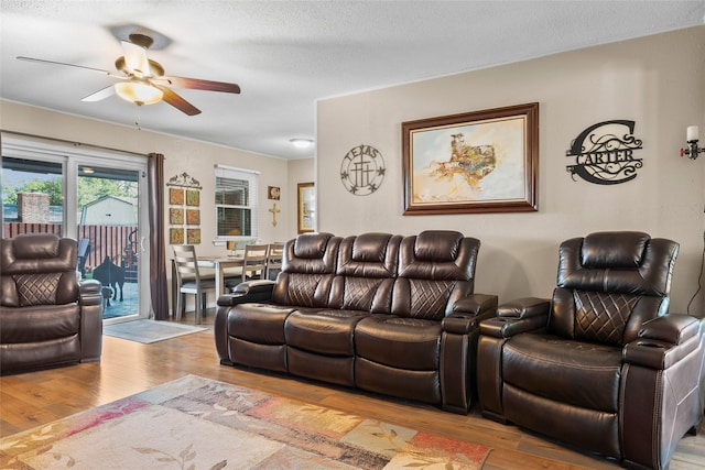 living area with a textured ceiling, light wood-style flooring, and ceiling fan