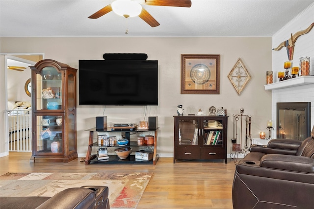 living room with a fireplace, ceiling fan, ornamental molding, and wood finished floors