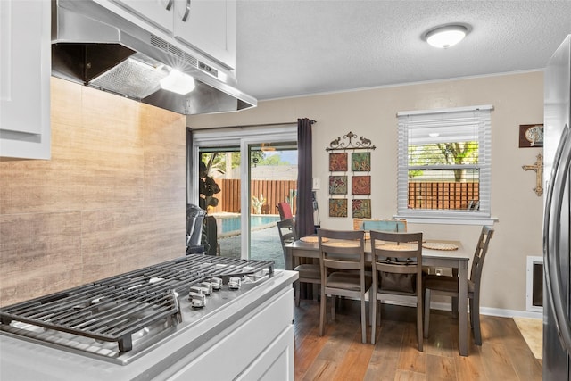 kitchen featuring a textured ceiling, under cabinet range hood, white cabinetry, crown molding, and light wood-type flooring