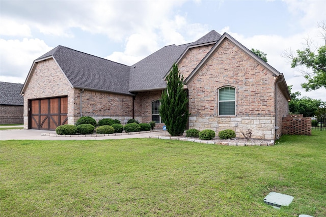 5807 Pebble Beach Dr, Granbury, TX 76049 - french country inspired facade with a shingled roof, brick siding, a front yard, concrete driveway, and an attached garage