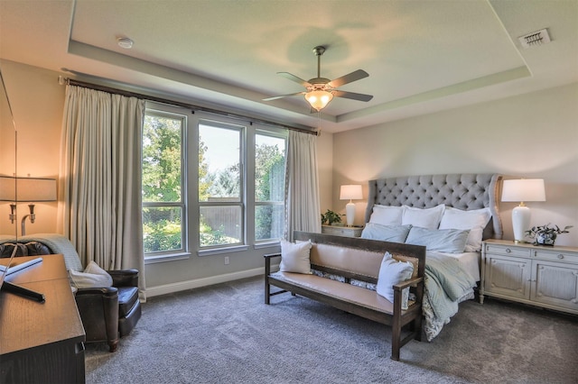 bedroom with a tray ceiling, multiple windows, visible vents, and dark carpet