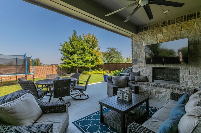 view of patio / terrace featuring a trampoline, outdoor dining space, a fenced backyard, a ceiling fan, and an outdoor living space with a fireplace