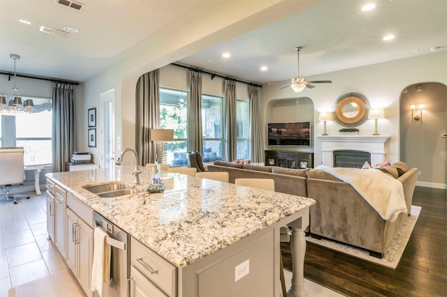 kitchen with a ceiling fan, a sink, a kitchen island with sink, light stone countertops, and a glass covered fireplace