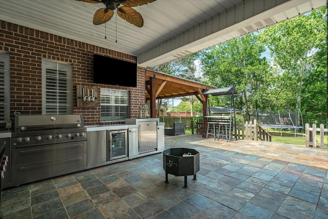 view of patio / terrace featuring a ceiling fan, an outdoor kitchen, beverage cooler, fence, and a trampoline