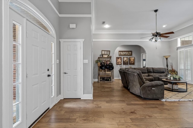 foyer entrance with ornamental molding, visible vents, ceiling fan, wood finished floors, and arched walkways